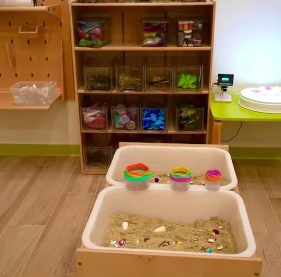 Sensory table filled with sand, scoops and colorful toys